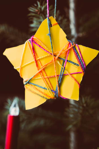 A beautiful yellow paper ornament, in the shape of a five pointed star, wrapped in some lovely multi-colored string to hang it on the tree.