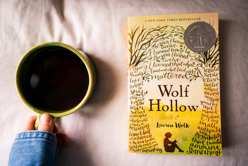 Wolf Hollow by Lauren Wolk paperback edition, with a cup of black coffee in a green ceramic mug crafted by a dear friend, Sarah.