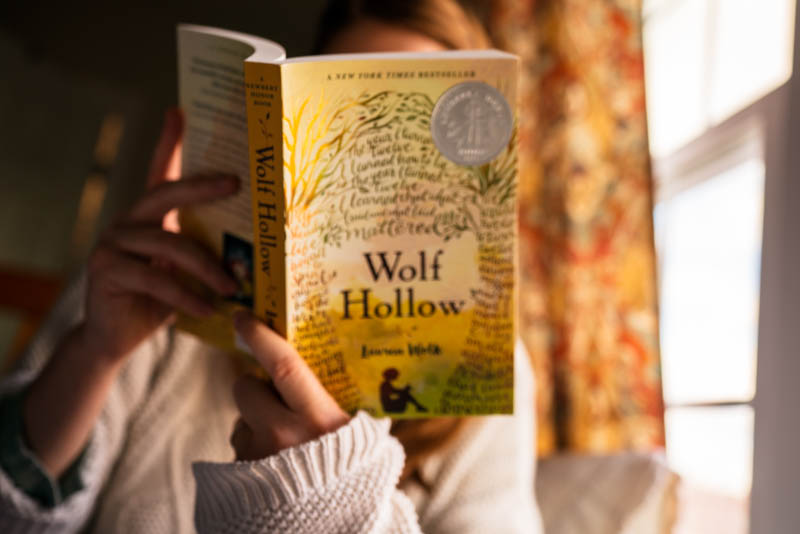 Reading the paperback print of Wolf Hollow by Lauren Wolk on a sunny afternoon.